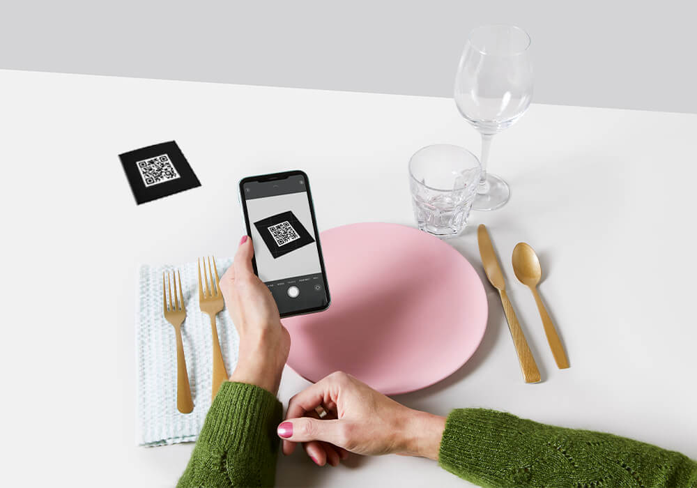 Frau sitzt an gedecktem Tisch und scannt einen QR-Code mit ihrem iPhone